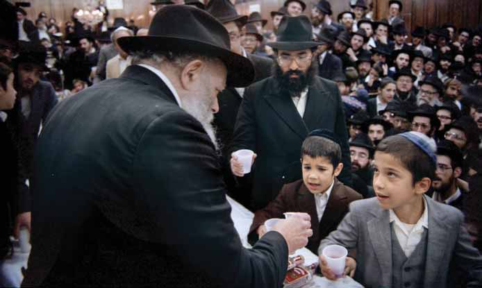 The Rebbe pouring kos shel bracha; two boys hold out cups while a bearded chassid stands behind them